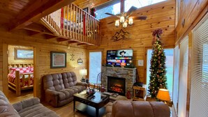 L’intérieur chaleureux d’un chalet en bois, avec une cheminée, un téléviseur et un sapin de Noël.