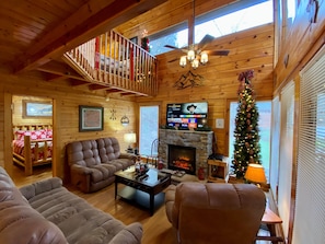 A cozy log cabin interior with a fireplace, a television, and a Christmas tree.