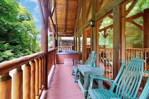 A wooden deck with a hot tub, wooden chairs, and a table.