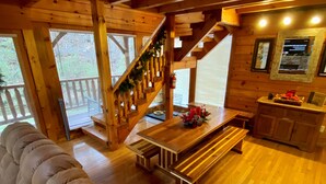 Un intérieur de chalet chaleureux avec un escalier en bois, un coin repas avec un banc et un espace salon avec des coussins.