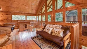 Une cabane au décor intérieur en bois, un canapé agrémenté de coussins à motifs et de grandes fenêtres offrant une vue sur la forêt.