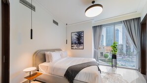 Ein modernes Hotelzimmer mit einem großen Bett, einem kleinen Beistelltisch, einer Topfpflanze und Blick auf die Stadt durch große Fenster.