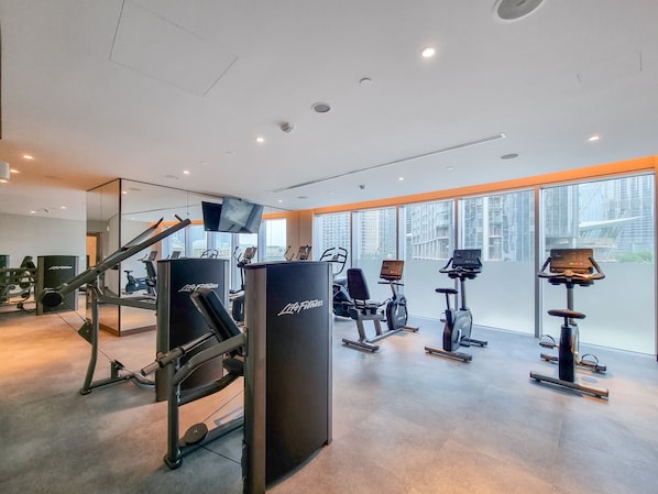 A gym with cardio machines, weight equipment, and large windows offering city views. - Charming 2BR Apt at Opera Grand (Dubai)