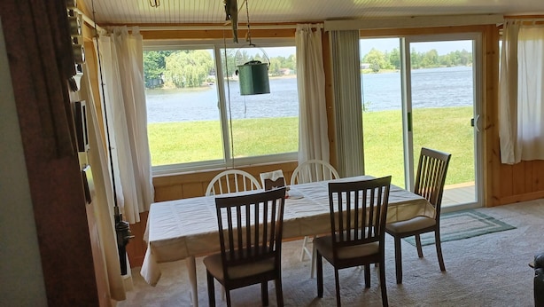 Un coin repas avec une table et des chaises, une vue sur un lac et une lampe sur une table d’appoint.