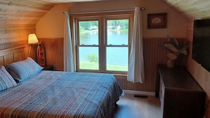 Une chambre à coucher avec un lit, une lampe, une fenêtre avec des rideaux et une vue sur un lac.