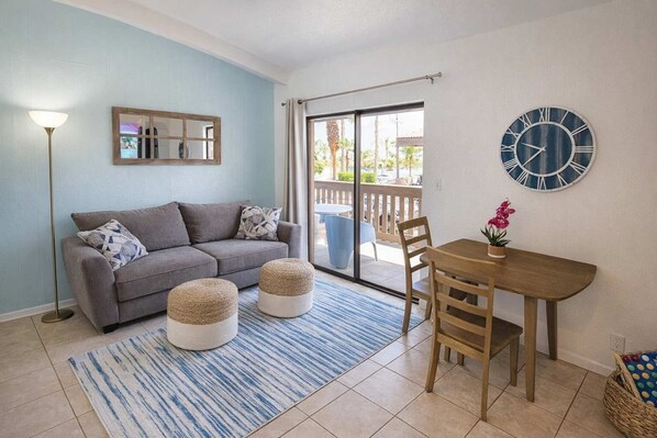 Un salon comprenant un canapé, des poufs, une table, des chaises, une horloge et une fenêtre.