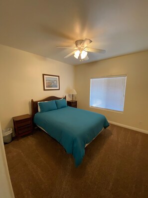 A bedroom with a bed, a nightstand, a lamp, a ceiling fan, a window with blinds, and a picture on the wall. - Seaside! Steps to sand & minutes to dunes! (Oceano)