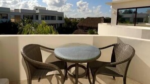 En balkon med et rundt bord og to fletstole, med udsigt over et boligområde med moderne bygninger og en klar himmel.