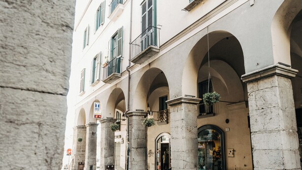 A building with arched windows and columns, a visible entrance, and hanging plants.