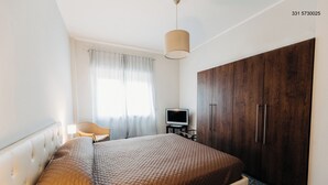 A bedroom with a bed, a television on a stand, a wardrobe, and a chair.