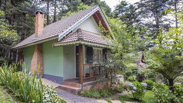 Uma casa com telhado de telhas, chaminé de tijolos e varanda com grade.