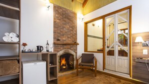 A cozy living room with a brick fireplace, wooden shelves, a comfortable chair, and a large window with a view.