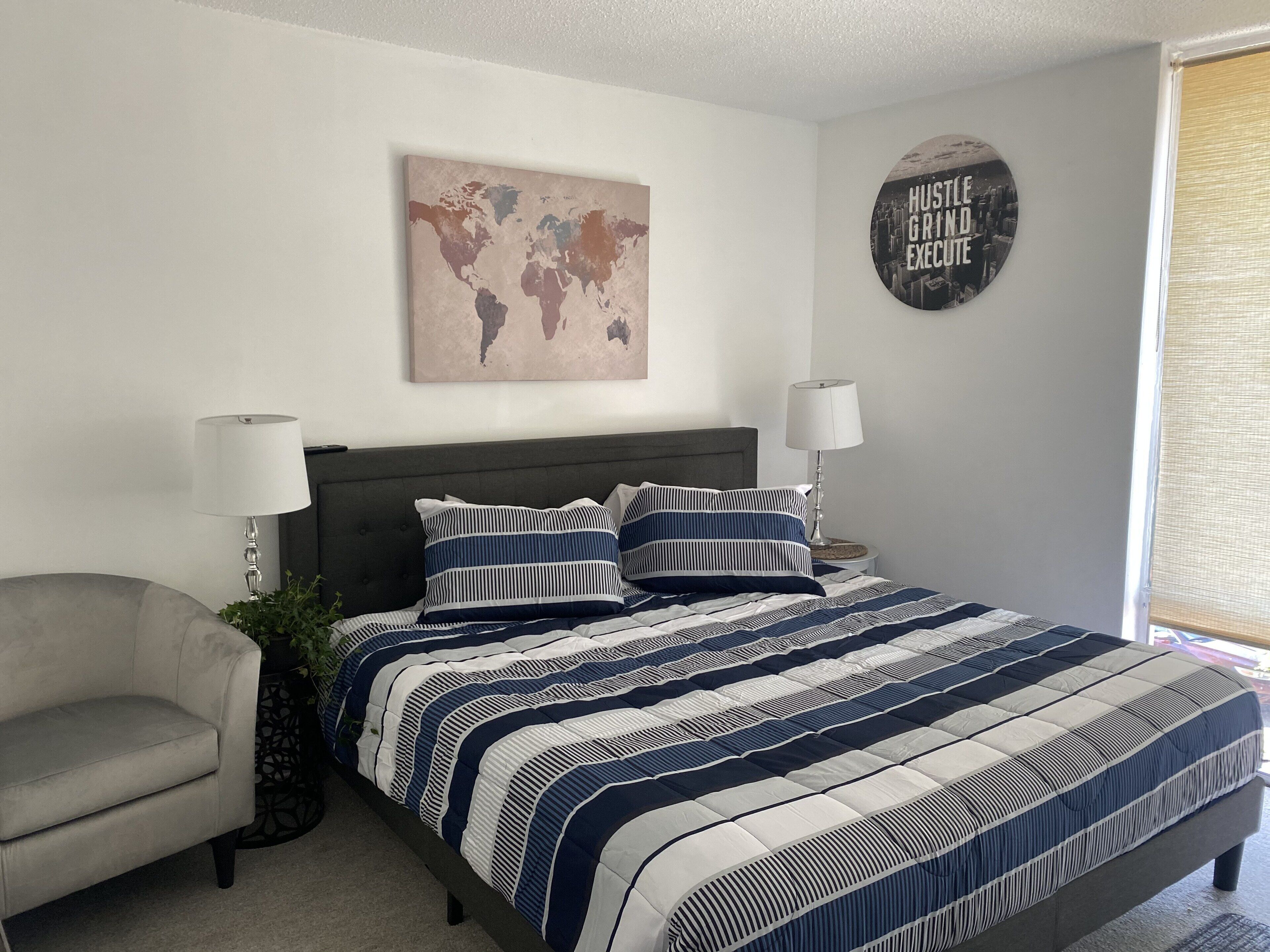 A bedroom with a bed, two bedside lamps, a world map on the wall, and a motivational quote.