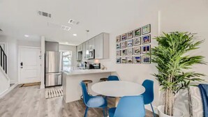 A modern kitchen with stainless steel appliances, a dining area with blue chairs, and a wall decorated with framed pictures.
