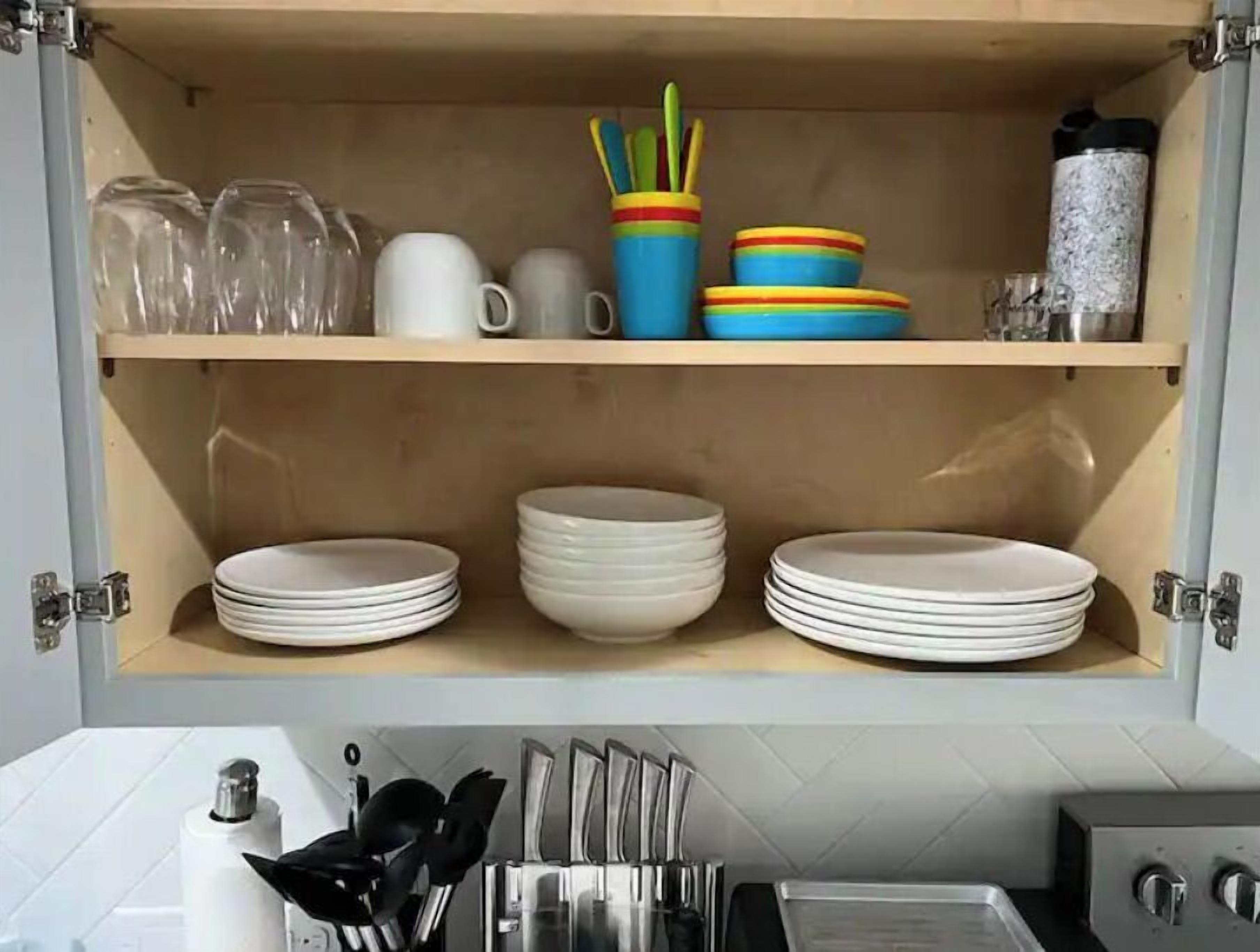 A kitchen cabinet with shelves holding glassware, mugs, and plates.