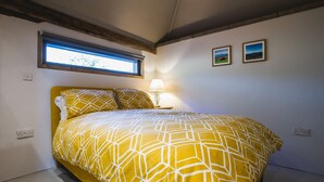 A bedroom with a bed, a window, a lamp, and two framed pictures on the wall.