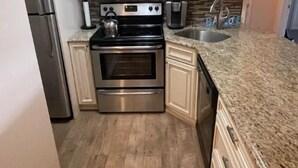 Una cocina con gabinetes blancos, electrodomésticos de acero inoxidable, encimera de granito y piso de madera.