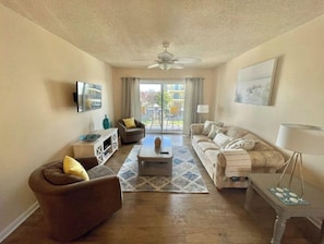 Ein Wohnzimmer mit Sofa, Sesseln, Couchtisch und einem an der Wand befestigten Fernseher.