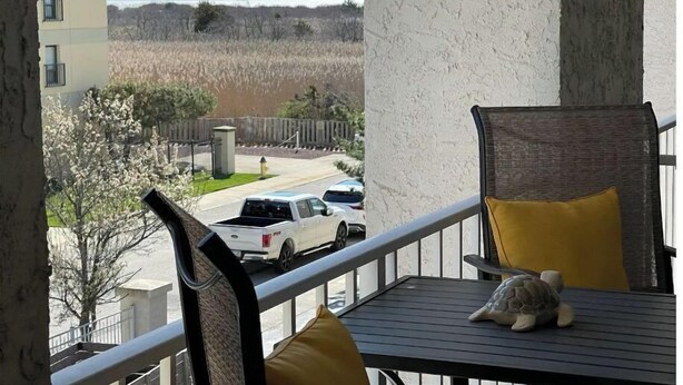Un balcón con vistas a un estacionamiento y un edificio. Hay una silla con cojín y una pequeña figurita de tortuga en la mesa.