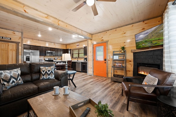 A cozy cabin interior with a living room, kitchen, and fireplace. - 5BR Cabin - Sleeps 12 - Hot Tub + Arcade - 10min to Dollywood (Sevierville)