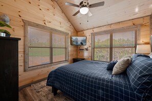 A bedroom with a bed, a ceiling fan, a TV, and wooden walls. - 5BR Cabin - Sleeps 12 - Hot Tub + Arcade - 10min to Dollywood (Sevierville)