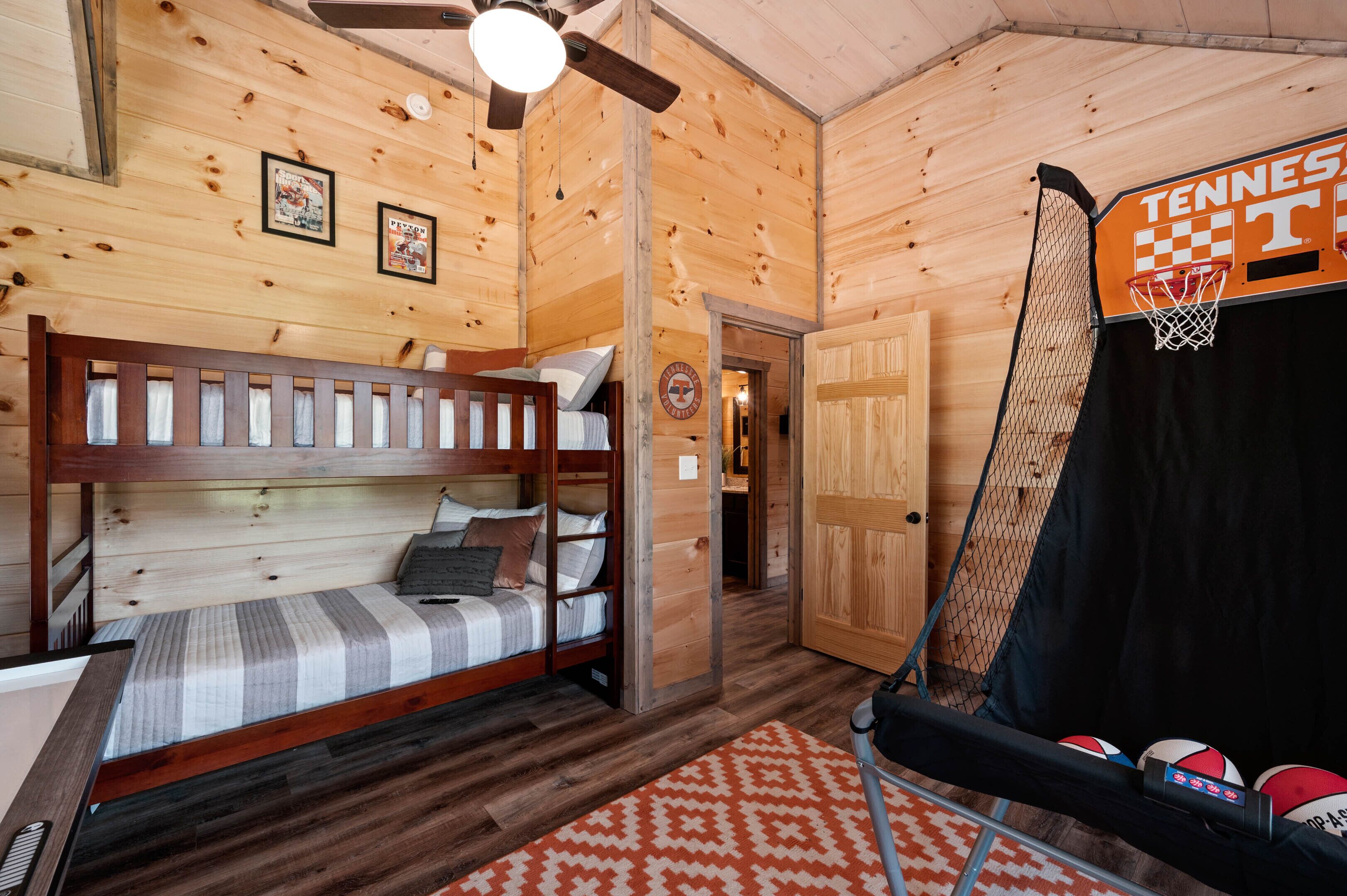 Interior d'una cabana de fusta amb un llit superposat, un cèrcol de bàsquet i una porta que dona a una altra habitació.