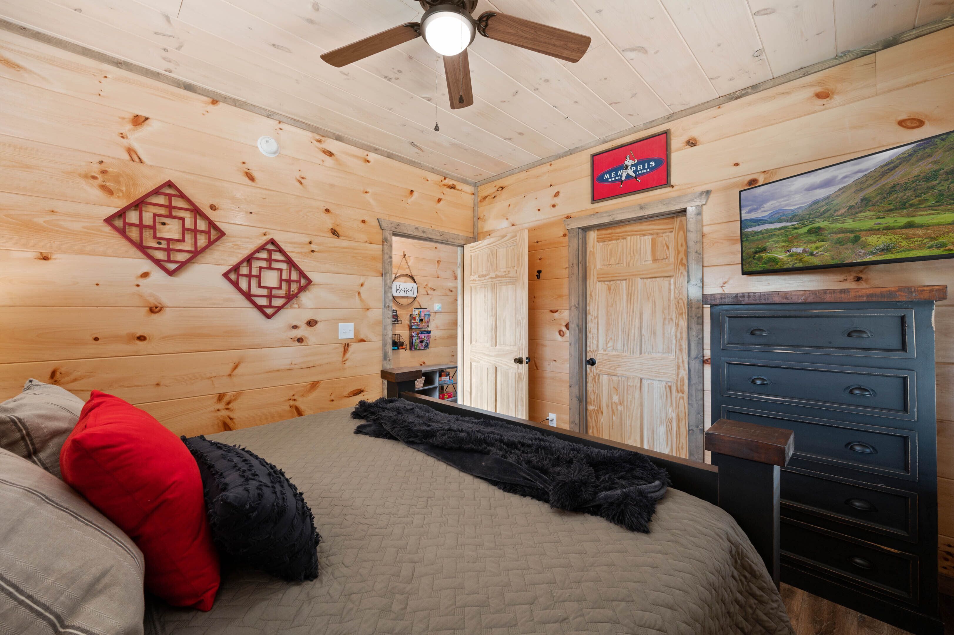 Ein Zimmer mit Holzwänden, einem Bett, einem Schminktisch, einem Fernseher und einem Deckenventilator.