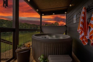 A hot tub on a balcony with a view of a field and a sunset. - 5BR Cabin - Sleeps 12 - Hot Tub + Arcade - 10min to Dollywood (Sevierville)