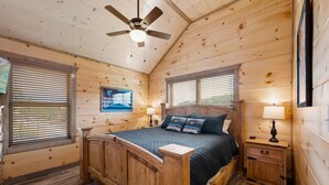 Une chambre dans une cabane en bois, avec un lit, deux tables de chevet, un ventilateur de plafond et une fenêtre avec des stores.