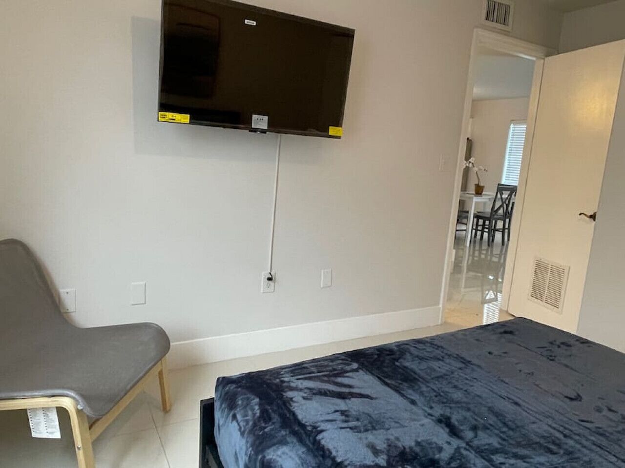 Ein Schlafzimmer mit einem Bett, einem Sessel, einem an der Wand befestigten Fernseher und einer Tür zu einem Badezimmer.