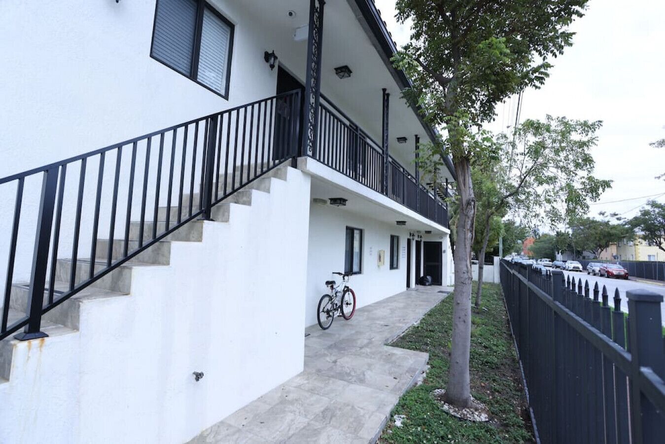 A two-story building with a white exterior, a black railing on the staircase, and a bicycle parked outside.