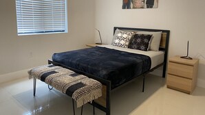 Quarto moderno com cama, mesas de cabeceira, um banco e janela com persianas.