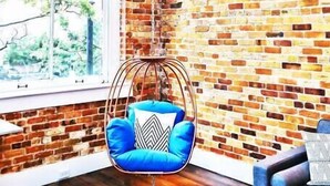 Une pièce avec un mur en briques, un fauteuil suspendu avec des coussins bleus et un canapé bleu.