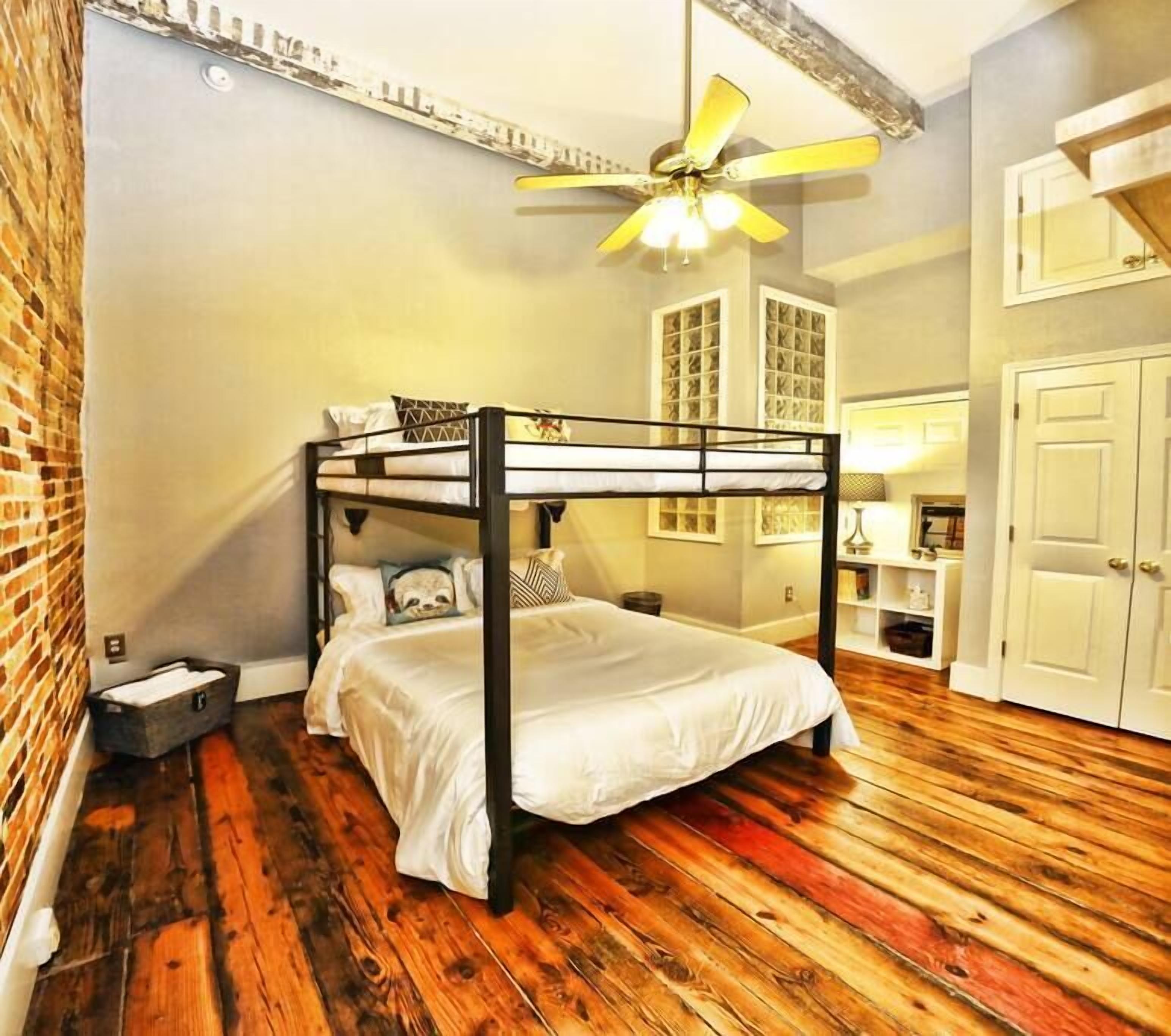 A bunk bed room with a wooden floor, a ceiling fan, and a brick wall.