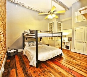 Ein Schlafraum mit Etagenbetten, Holzboden, Deckenventilator und Backsteinwand.