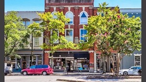 Une vue de rue avec un immeuble en briques rouges, des devantures de magasins et des voitures garées.