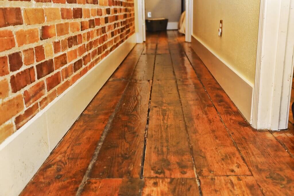 A narrow hallway with wooden flooring and a brick wall on one side.
