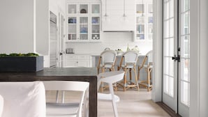 A modern kitchen with white cabinetry, a dining area with a wooden table and white chairs, and a large window with a view of the outside. -  #1 VRBO in Austin HEATED POOL, central to 6th and Rainey (Austin)