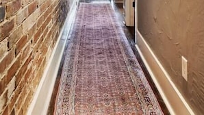 Un passadís estret amb una paret de maó d'un costat i una paret amb relleu de l'altre, que condueix a una habitació amb finestra i escriptori.