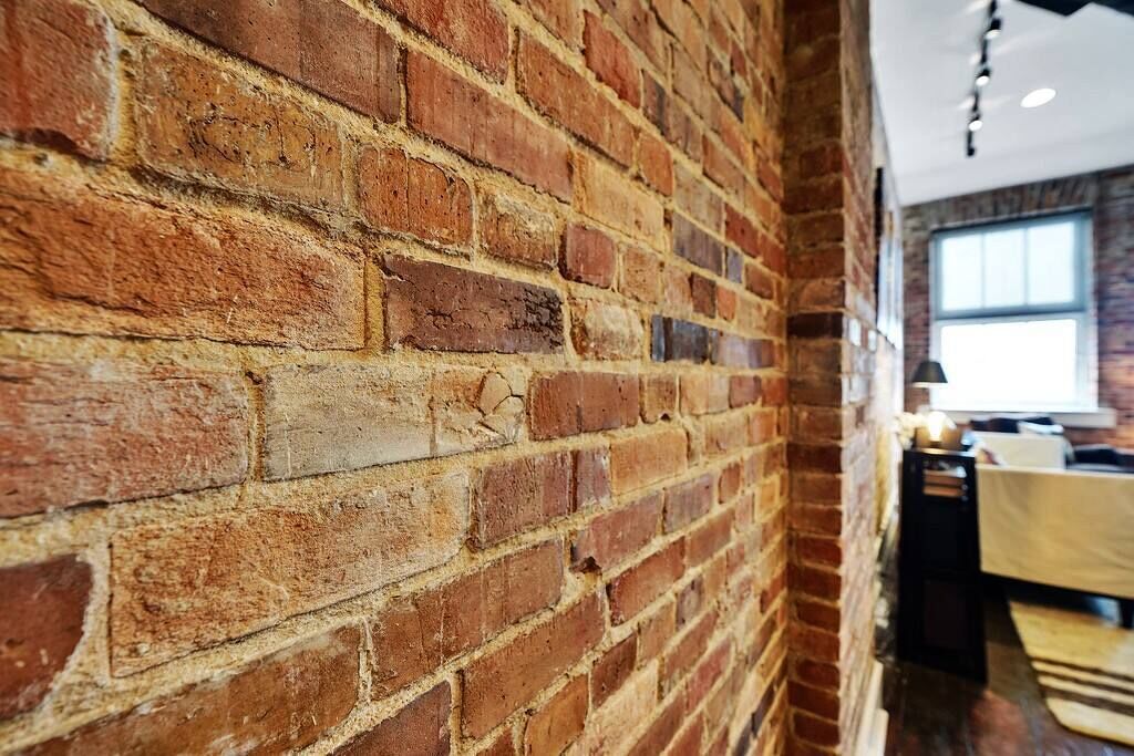 A brick wall in a room with a window and a table with a lamp.