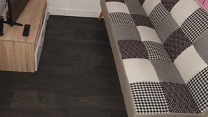 Ein modernes Wohnzimmer mit dunklem Holzboden, einer Couch mit gemusterten Kissen, einem Fernseher auf einem Holzschrank und einer roten Wand.