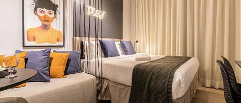 A modern hotel room with a bed, a sofa, a table with a glass, and a painting on the wall.