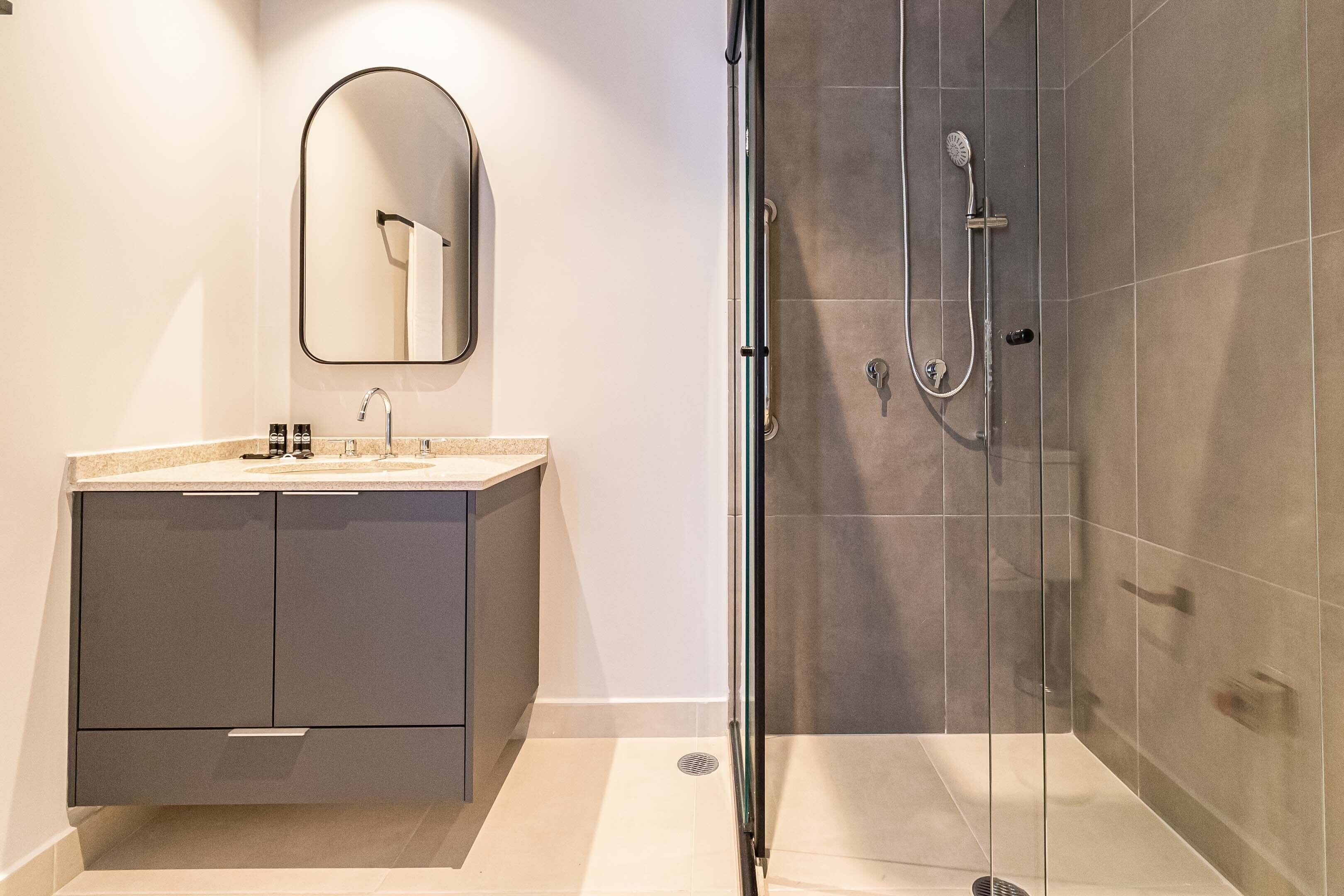 Un baño moderno con cabina de ducha de vidrio, un lavabo con espejo y un mueble de baño con armarios.