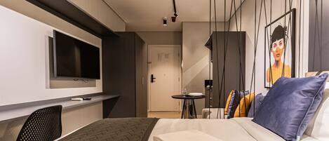 A modern hotel room with a bed, a TV, a desk, and a small table with a chair.