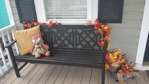 A wooden bench with a cushion and a fox plush toy on a porch with a lattice railing and a window with blinds. - Historic Home - minutes from Downtown and Beach! (Pensacola)