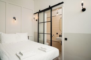 A hotel room with a bed, a sliding door to the bathroom, and wall-mounted lights. - Mr.Lewis Hotel Rotterdam (Rotterdam)