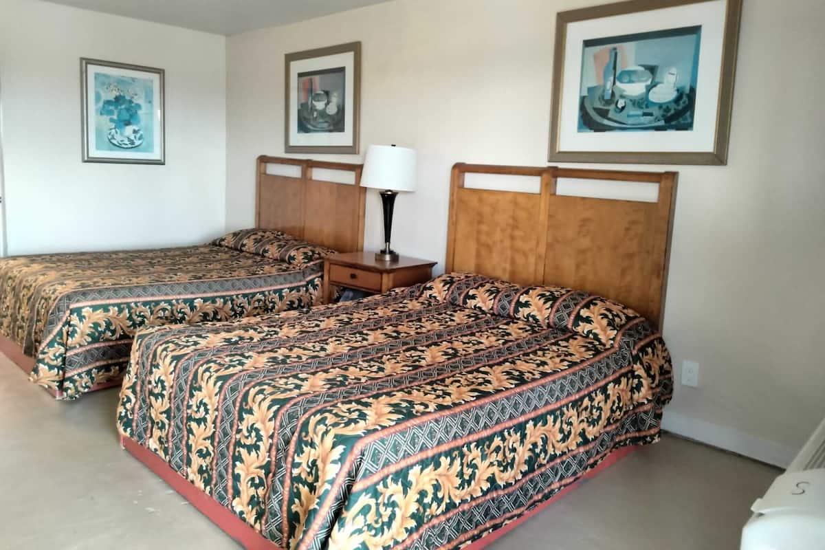 A hotel room with two beds, each with patterned bedding, a nightstand with a lamp, and framed artwork on the walls.