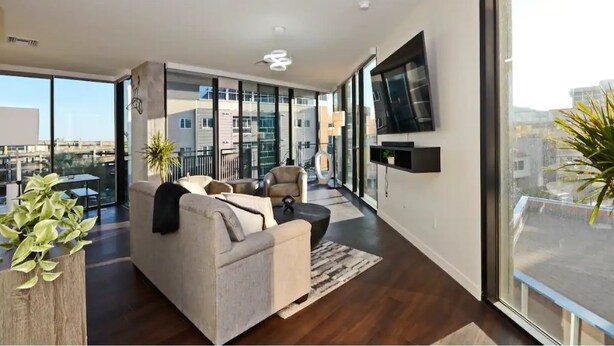 A modern living room with a sofa, chairs, a coffee table, and a TV mounted on the wall. - Luxury High Rise Flat - Free Underground Parking (Tucson)