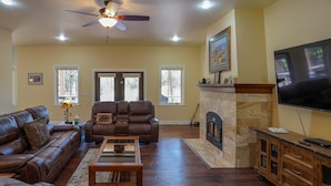 A living room with a fireplace, leather sofas, a television, and a ceiling fan. - AMAZING 4300 SQ FEET RETREAT ON  4.5 ACRES WITH AC!! SLEEPS 16 PETS WELCOME! (Pinetop-Lakeside)