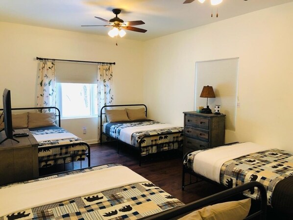 A bedroom with three single beds, a ceiling fan, a window with curtains, and a bedside lamp.